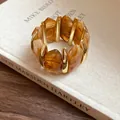 Makro-Detail eines unregelmäßigen elastischen Armbands aus bernsteinfarbenem Acryl und Gold - Dunkelkaffee