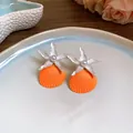 Close-up detail of vibrant orange shell earrings with white starfish and pearl accents. - White-Orange