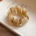 Nahaufnahme von marmorierten Acrylsegmenten mit goldfarbenen Metallstäben am Armband - Hellkaffee