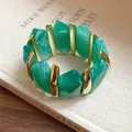 Detailansicht eines grünen elastischen Acryl-Armbands mit goldenen Metallelementen. - Grün