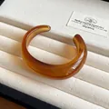 Detailed macro shot of an amber marbled acrylic open bangle displayed on a soft cream jewelry tray - Amber