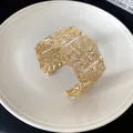 Primer plano de un brazalete ancho dorado con intrincados patrones florales huecos - Dorado