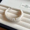 Detailed close-up view of a cream marbled acrylic open cuff bracelet texture - White