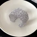 Primer plano del intrincado diseño floral calado en este brazalete ancho plateado - Plateado