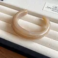 Macro view of a light brown marbled acrylic open bangle on a cream velvet display tray - Brown