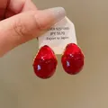 Close-up of teardrop-shaped red resin earrings with gold wire detail on a white tag. - Red