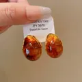 Macro view of vintage amber teardrop earrings with S925 silver needle on a white export tag - Brown