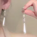 Close-up detail of French silver needle earrings with long white teardrop pearls - Style 7 (Stud) / Gold-White