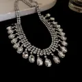 Detailed macro shot of vintage-inspired square rhinestone fringe necklace on black surface. - Silver
