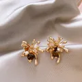 Macro detail of gold-plated floral earrings with pearls and crystals on champagne satin - Radiant Flower Style / Gold