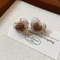 Detailansicht der herzförmigen Ohrstecker mit braunem Harz und Tweed-Stofftextur - Kaffee-Weiß