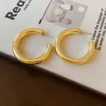 Detail of minimalist gold-plated C-shaped chunky hoop earrings on a magazine background - Diameter 39mm / Gold