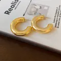Close-up of polished gold-plated chunky C-shaped hoop earrings on a book - Diameter 38mm / Gold