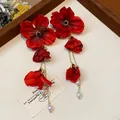 Close-up of elegant red fabric flower earrings with gold tassel and pearl drops - Red