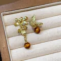 Detailed view of asymmetric earrings with gold flowers, butterfly, and amber beads - Gold Brown