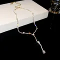 Close-up of sparkling silver teardrop zircon tassel necklace on white display box - Gold