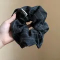 Detailed macro view of a dark grey striped fabric scrunchie with brand label - Gray