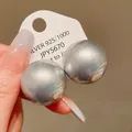 Macro shot of oversized silver-colored round stud earrings on a white display card. - Gray