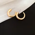 Close-up detail of golden chunky hoop earrings with high-gloss polished finish. - Gold Chunky Tube C-Shape