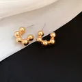 Close-up detail of elegant gold-tone beaded C-shaped hoop earrings on fabric - Gold Beaded C-Shape