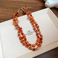 Detailed view of the double-layered irregular orange shell bead necklace with gold accents. - Brown
