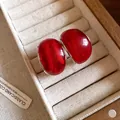 Primer plano de pendientes de resina roja brillante en un joyero de terciopelo y madera - Rojo