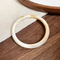 Close-up of a vintage acrylic acetate bangle with beige marble pattern on wooden texture - Off White