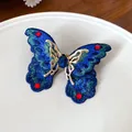 Primo piano di anello a farfalla ricamato con gemma blu e strass rossi scintillanti. - Stile Farfalla Aperta (WR385) / Oro-Blu-Verde