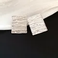 Macro detail of silver-toned rectangular earrings with a unique wrinkled texture design - Silver