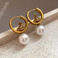 Close-up of vintage gold Saturn orb hoop earrings with elegant imitation pearl drops - Letter Saturn Buckle / Gold-White