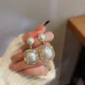 Primo piano di orecchini vintage in perle con bordo in strass tenuti in mano. - Ciondolo di Perla (No.1)