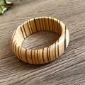 Close-up of a vintage wooden bangle with vertical stripe patterns on a wood background - Style 6
