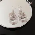 Detailansicht von silbernen runden Hohl-Quastenohrringen auf einer Spiegelfläche. - Ohrhaken / Silber