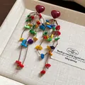 Close-up of bohemian heart earrings with vibrant colorful shell tassel strands - Colorful