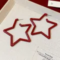 Detailed macro shot of elegant red star-shaped hoop earrings on beige fabric base - Star / Red
