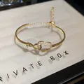 Close-up of gold heart bangle with pavé-set zircons and adjustable infinity chain link - Hollow Heart Style / Gold