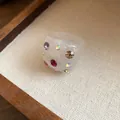 Detailed view of a white resin ring with vibrant multi-colored embedded rhinestones. - Clear