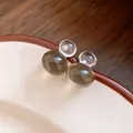 Macro detail of minimalist resin gourd-shaped earrings in amber and clear jelly colors on a plate - Gourd (HE22133) / Gray
