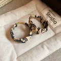 Close-up of stylish fabric-wrapped hoop earrings with black artistic paisley patterns. - White