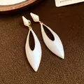 Close-up of retro white enamel hollow water drop earrings with golden frame detail. - Beige