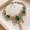 Macro view of vintage gold-toned necklace with green water-drop gems and rhinestones - Necklace / Gold-Green