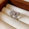 Macro view of an elegant silver bow-shaped open ring with pavé-set zircons in a box. - Silver