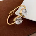 Detail of a gold-plated open cuff bracelet featuring two large round-cut clear crystals - Gold