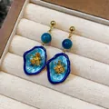 Close-up detail of vintage blue enamel flower earrings with stone bead and gold accents - Blue