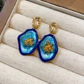 Detailed close-up of vintage blue enamel floral earrings with gold core in jewelry box - Gold & Blue