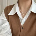 Collier de perles minimaliste avec pendentif doré porté sur un gilet marron. - 38# Collier - Style Superposé en Perle avec Boucle en Strass