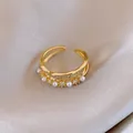 Vista macro di un anello a doppia fascia dorata decorato con perle e pietre di zircone lucide. - Stile Fluido Perla Artificiale Zirconia Doppio Strato