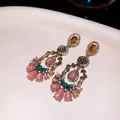Close-up detail of ornate vintage chandelier earrings with pink resin and green stones - Bronze-Green-Pink