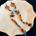 Dettaglio orecchini boho lunghi con perline colorate e pietre naturali su piatto bianco - Colorato