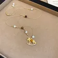 Détail d'un collier cheval à bascule doré avec perles et strass sur un plateau beige - Brun doré